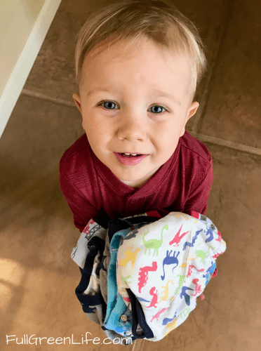 2 year old boy holding clean laundry in arms and looking proud