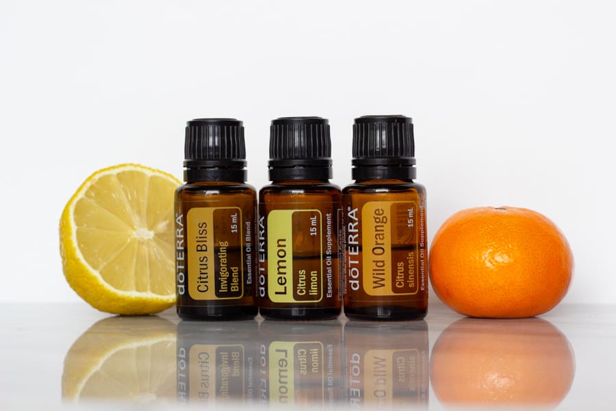 bottles of doterra citrus bliss, lemon, and wild orange pictured beside a half of a lemon and a small orange